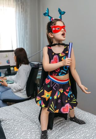 Girl in disguise singing and dancing on the bed while her mother works from home