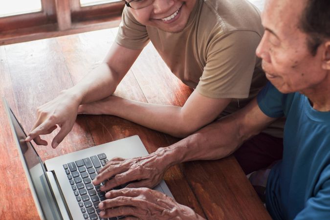 Happy adult son teaching older father using laptop