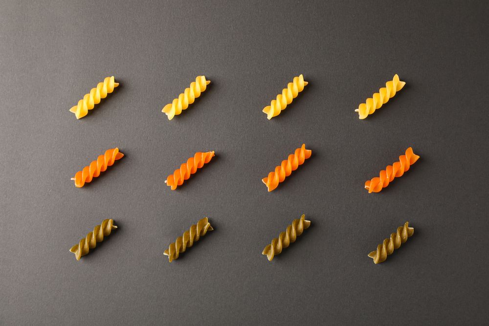 Flat lay composition with multicolored pasta on dark background, space for text