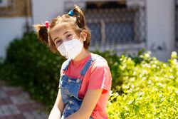 Female child in facemask next to bush outside