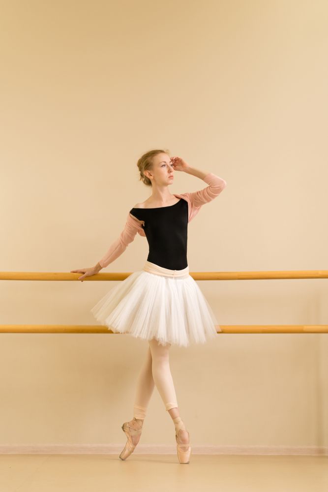 Focused ballerina stands gracefully on pointe, holding barre