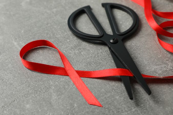 Awareness red ribbon and scissors on grey background, copy space