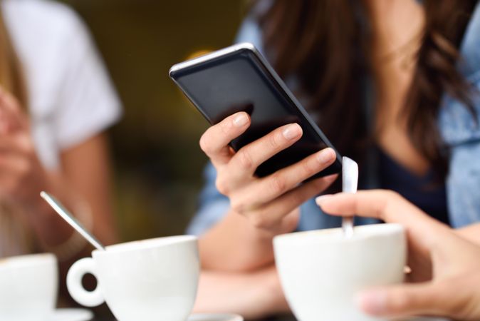 Hands of female typing text message on cellphone with coffee
