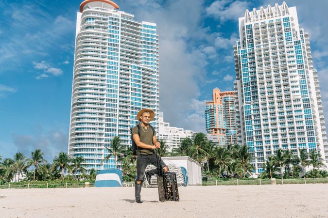 man with luggage bag on wheels standing on the south beach in miami.