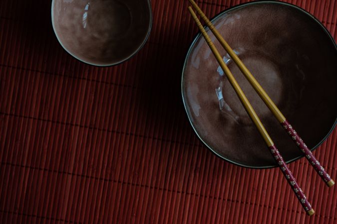 Two ceramic bowls with chopsticks on red table mat