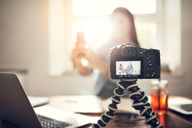 Woman filming herself in her bright home office holding cell phone