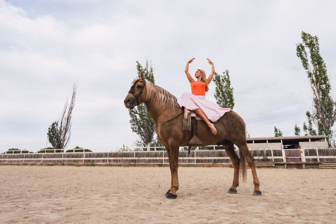Graceful rider sitting at harnessed horse walking along paddock