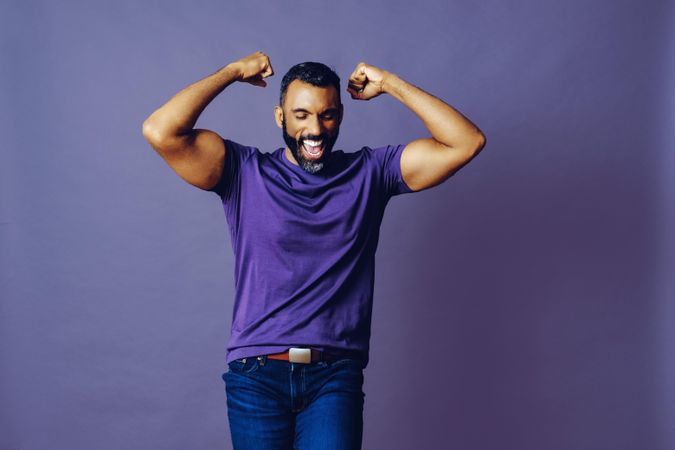Proud smiling male flexing his bicepts in celebration in purple studio, copy space