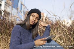 Curious female in hat and sweater sitting outside with tablet, copy space 5QvMG4