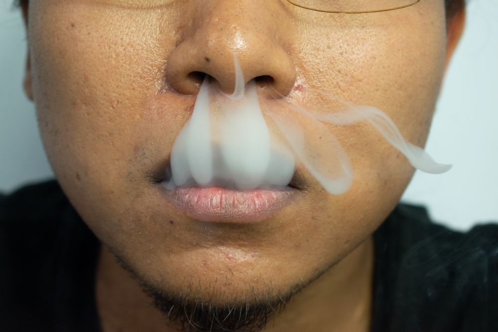 Face of man exhaling cigarette smoke from mouth