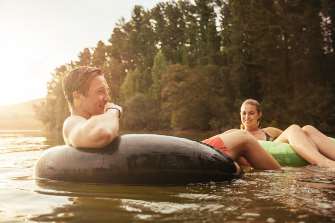 Portrait of happy young man in lake on inflatable ring with his girlfriend