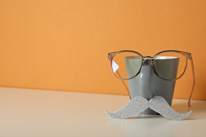 A cup with a mustache and glasses, on an orange background.