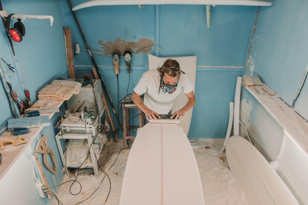 Man in respirator polishing surf board in workshop