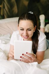 Smiling woman using tablet on bed in bedroom