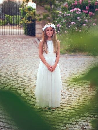 Smiling girl in white dress in park standing on pavement near tr
