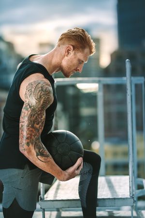 Side view of a man in fitness wear training on rooftop holding a medicine ball