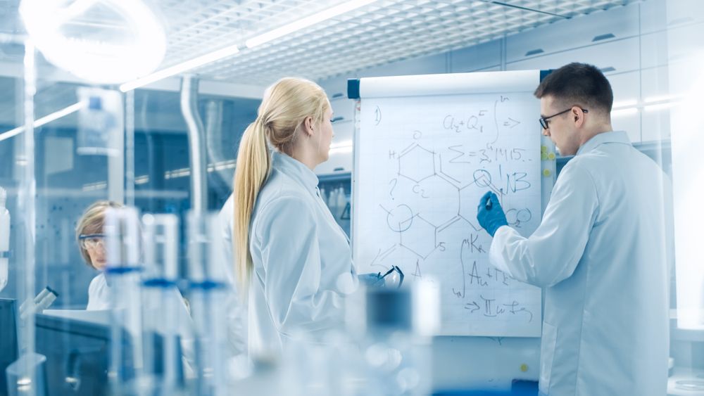 Young Female and Male Scientists Write Formulas on a Whiteboard.