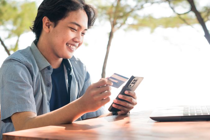 Happy Asian Young businessman hold blue creditcard and phone purchasing online shopping in outdoor cafe.