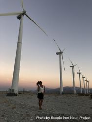 Woman standing on brown sand near wind turbines at sunset bGQQA5