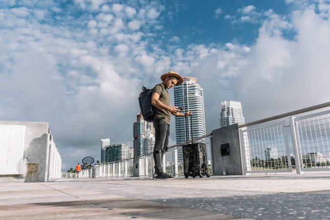 Full length photo of a man checking his smartphone standing with his suitcase.