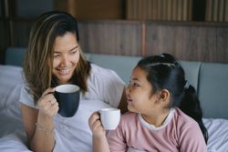 Mother and daughter having a morning hot drink in bedroom