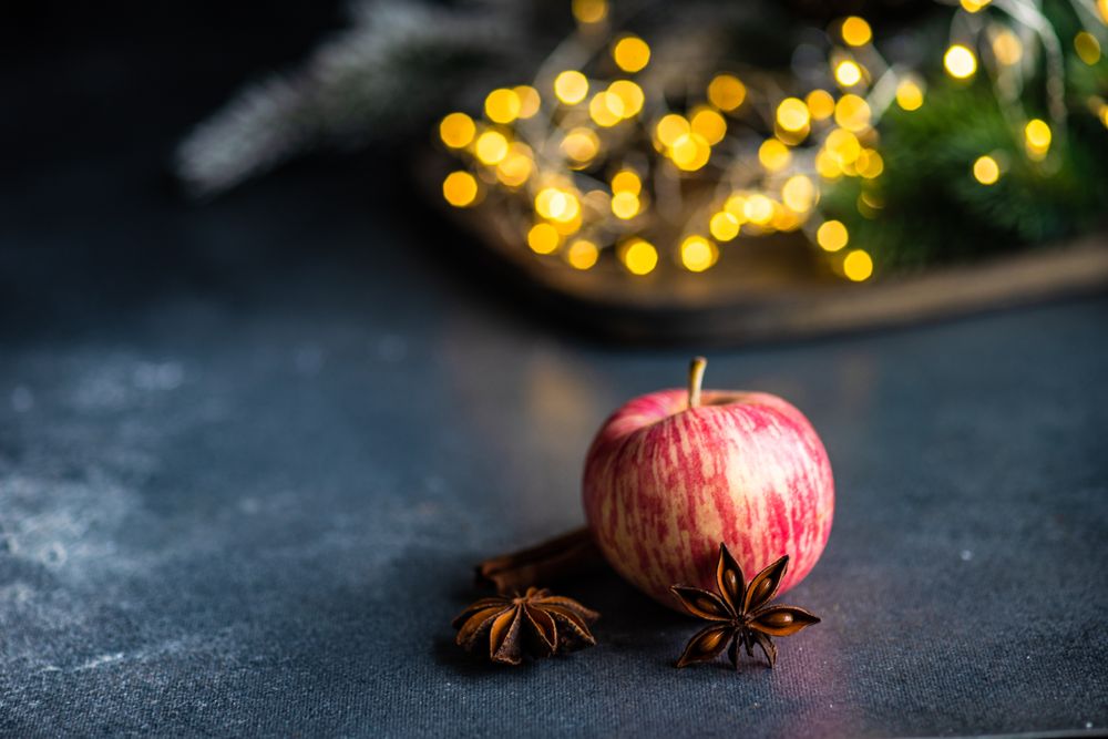 Apple on table with star anise and cinnamon stick with Christmas lights in background