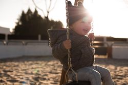 Young boy in blue denim jacket sitting on swing