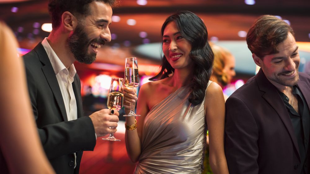 Multiethnic Couple Having a Fun Conversation at a Casino while Drinking Champagne and Gambling at a Roulette Table.