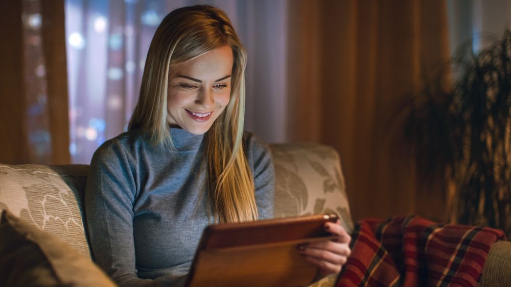 Young Woman in Her Living Room. She is Sitting on a Sofa and Uses Tablet Computer.