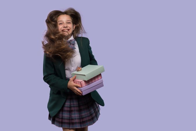 Schoolgirl holds colorful gift boxes with hair blowing in wind.