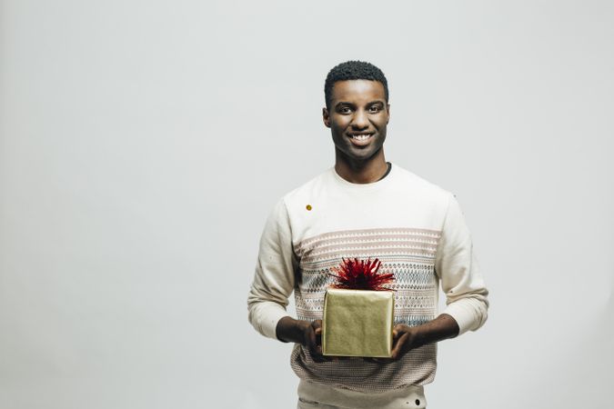 Smiling Black man holding a wrapped present in a bright room
