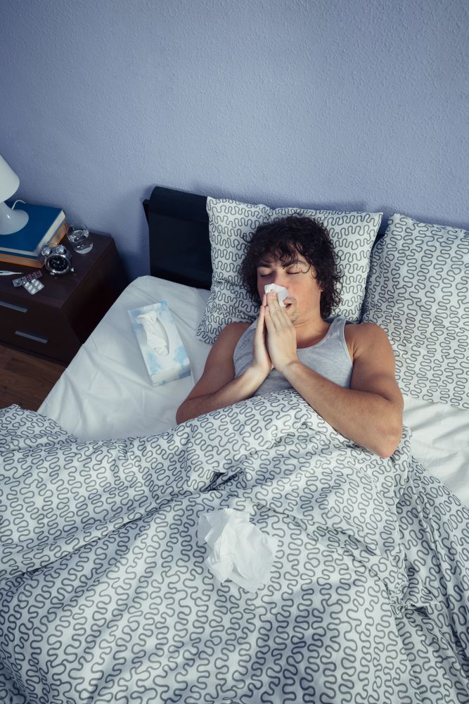 Looking down at ill man sneezing and blowing nose with tissue