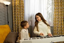 Girl in glasses plays digital piano while boy watches curiously.