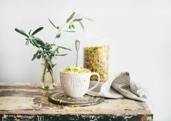 Cup of pistachio ice cream with spoon, on wooden table with leaves, and table linen
