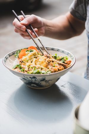 Man eating noodles at Vietnamese restaurant with chopsticks