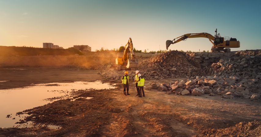 Aerial Drone Shot Of Construction Site With Excavators On Sunny Day: Diverse Team of Real Estate Developers Discussing Project. Engineer, Architect, Investor Talking About New Building, Using Tablet.
