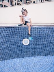 Puzzled boy in diving mask and flippers over empty pool