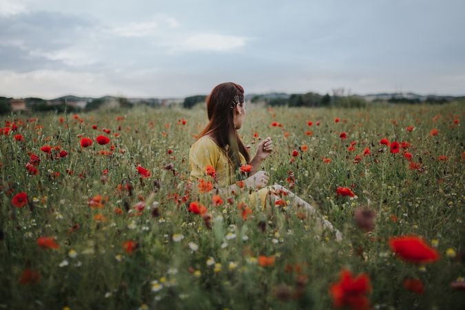 Woman sitting in field with poppies and daisies