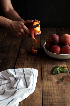 Tasty ripe peaches in plate and hands peeling peach