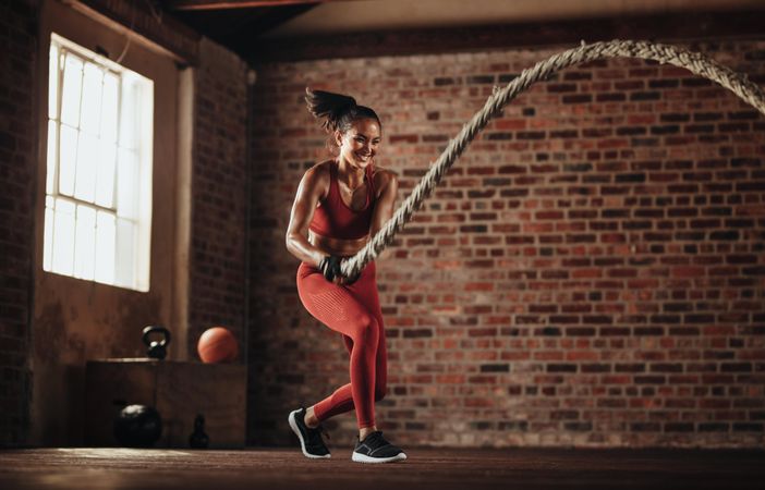 Strong female athlete working out with battling rope at gym