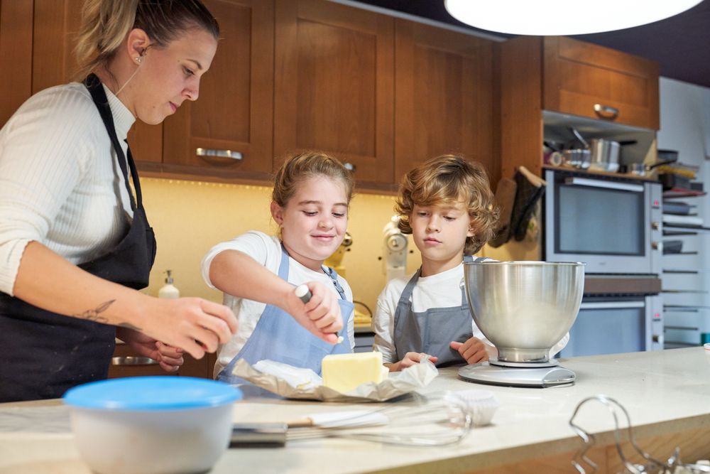 Girl with an apron cutting a piece of butter with a boy and a woman next to her