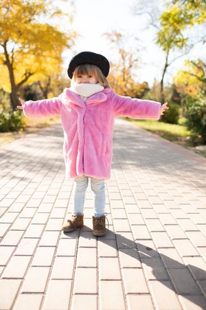 Girl in fluffy autumn coat opening her arms standing in park