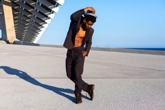 Front view of Black bearded man holding head while dancing against blue sky on a sunny day