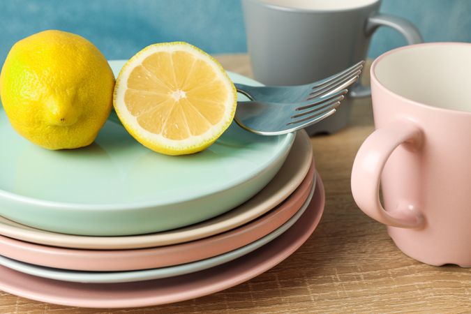 Plates and cups with lemons stacked on wooden table, close up