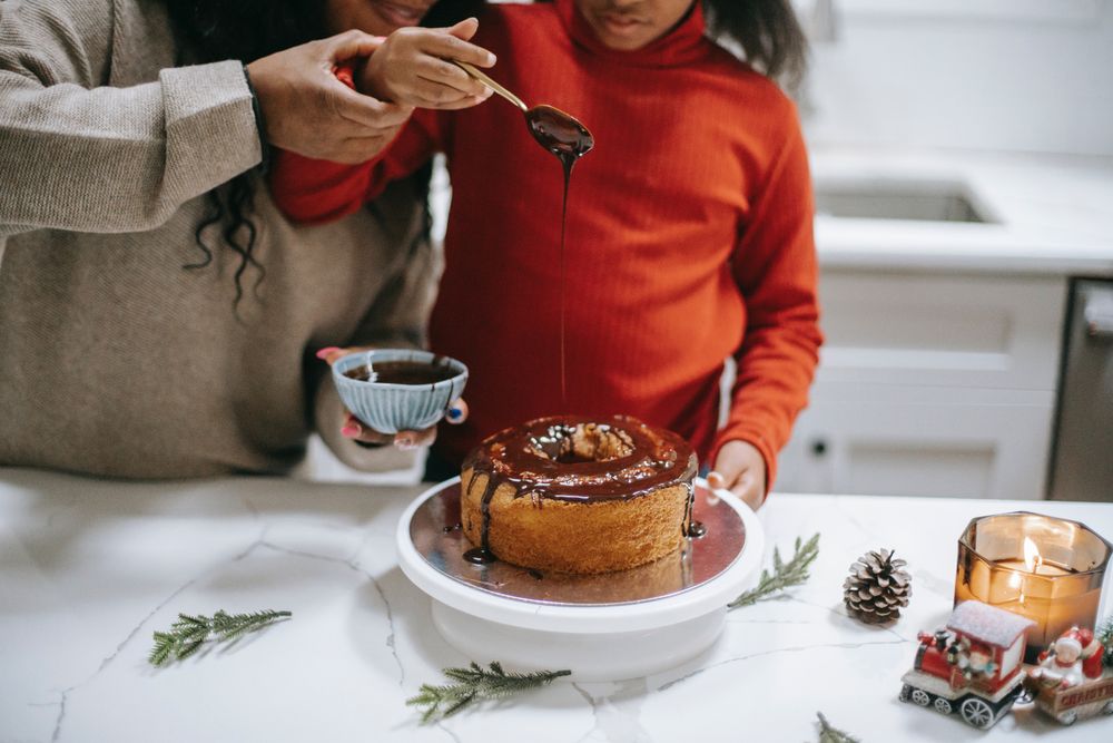Cropped image of mother helping daughter adding chocolate topping on a cake