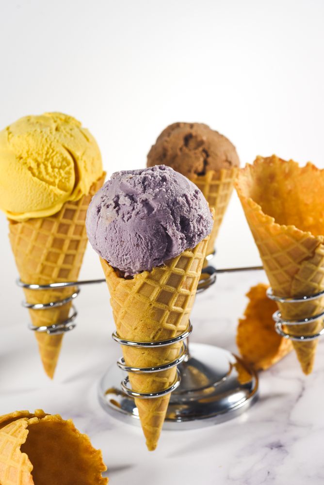 Close up of ice cream cone stand with waffle cones and three different scoops