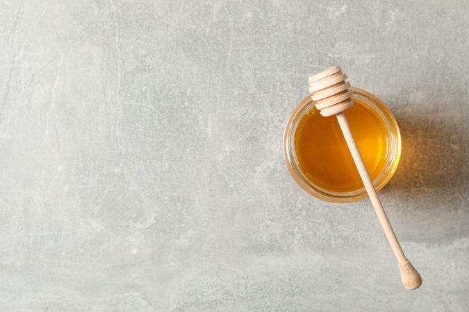 Glass jar with honey and dipper on grey background, copy space