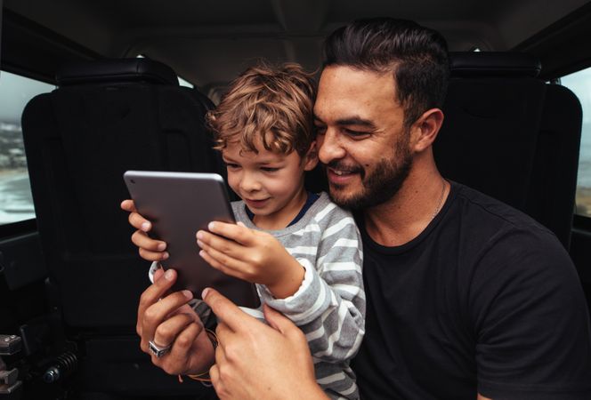 Young man and little boy using digital tablet while on road trip