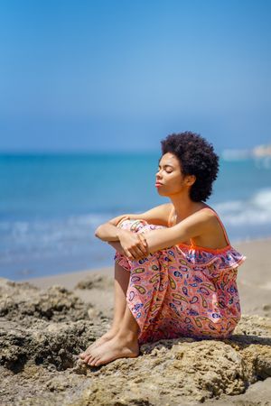 Woman with eyes closed sitting on the rocks on the coast by the sea, vertical