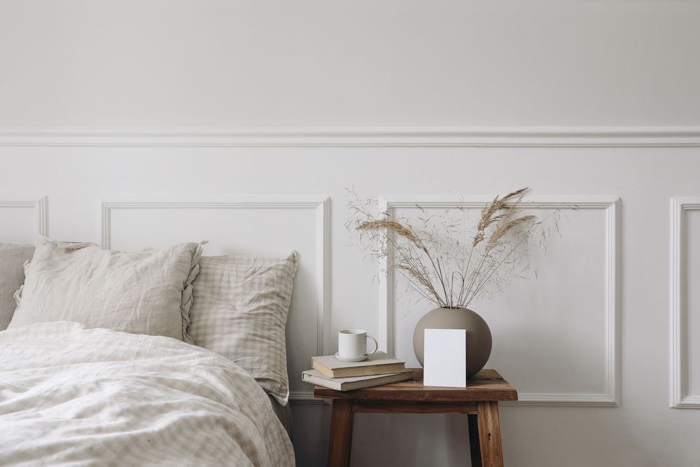 Bedside table with mockup frame and vase next to comfortable bed